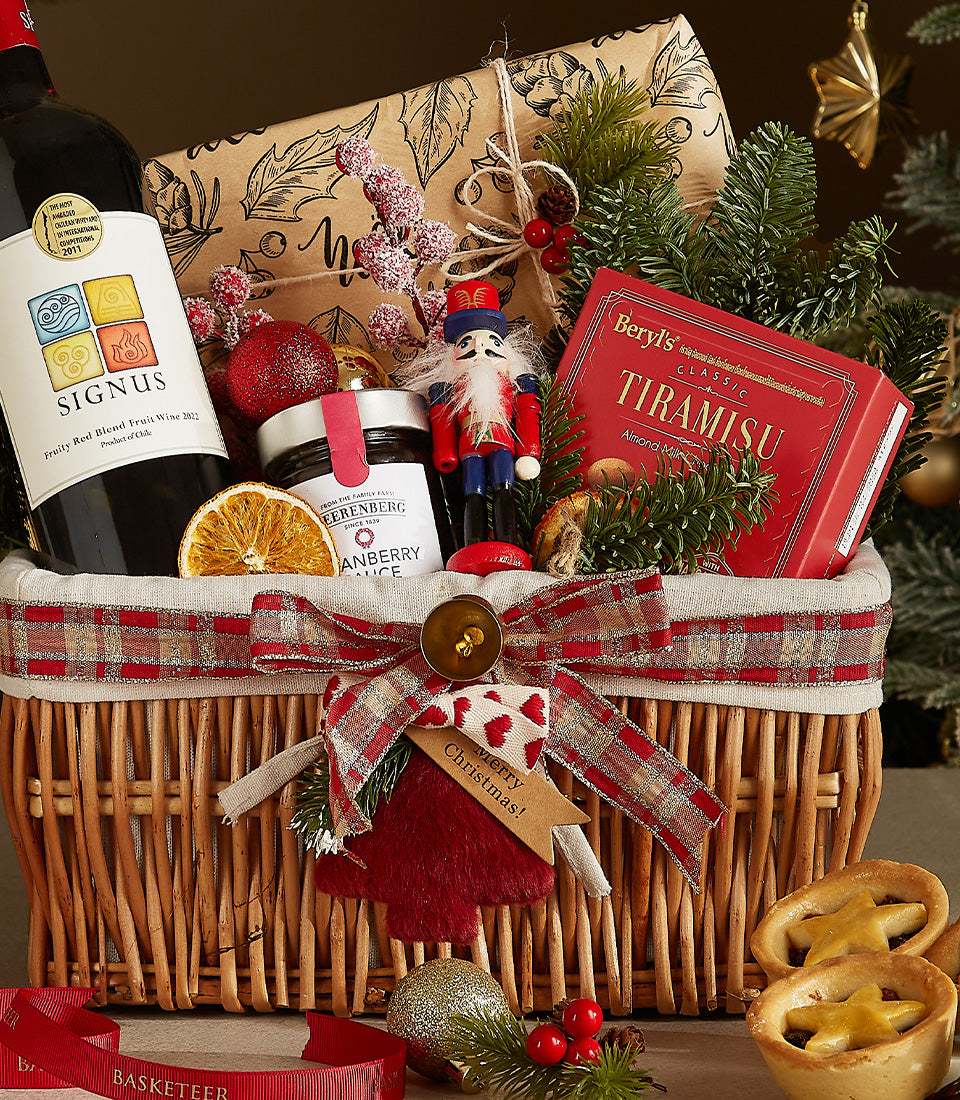 Festive wicker wine gift basket with red plaid bow, red wine, cranberry sauce, tiramisu, and Christmas ornaments
