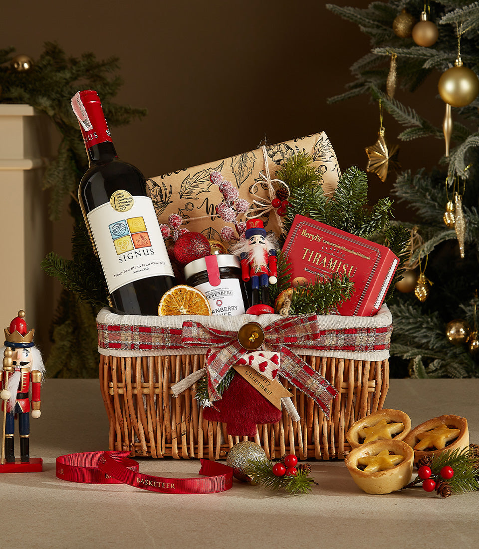 Woven wicker Christmas wine gift basket with red wine, cranberry sauce, tiramisu, mince pies, and festive decorations