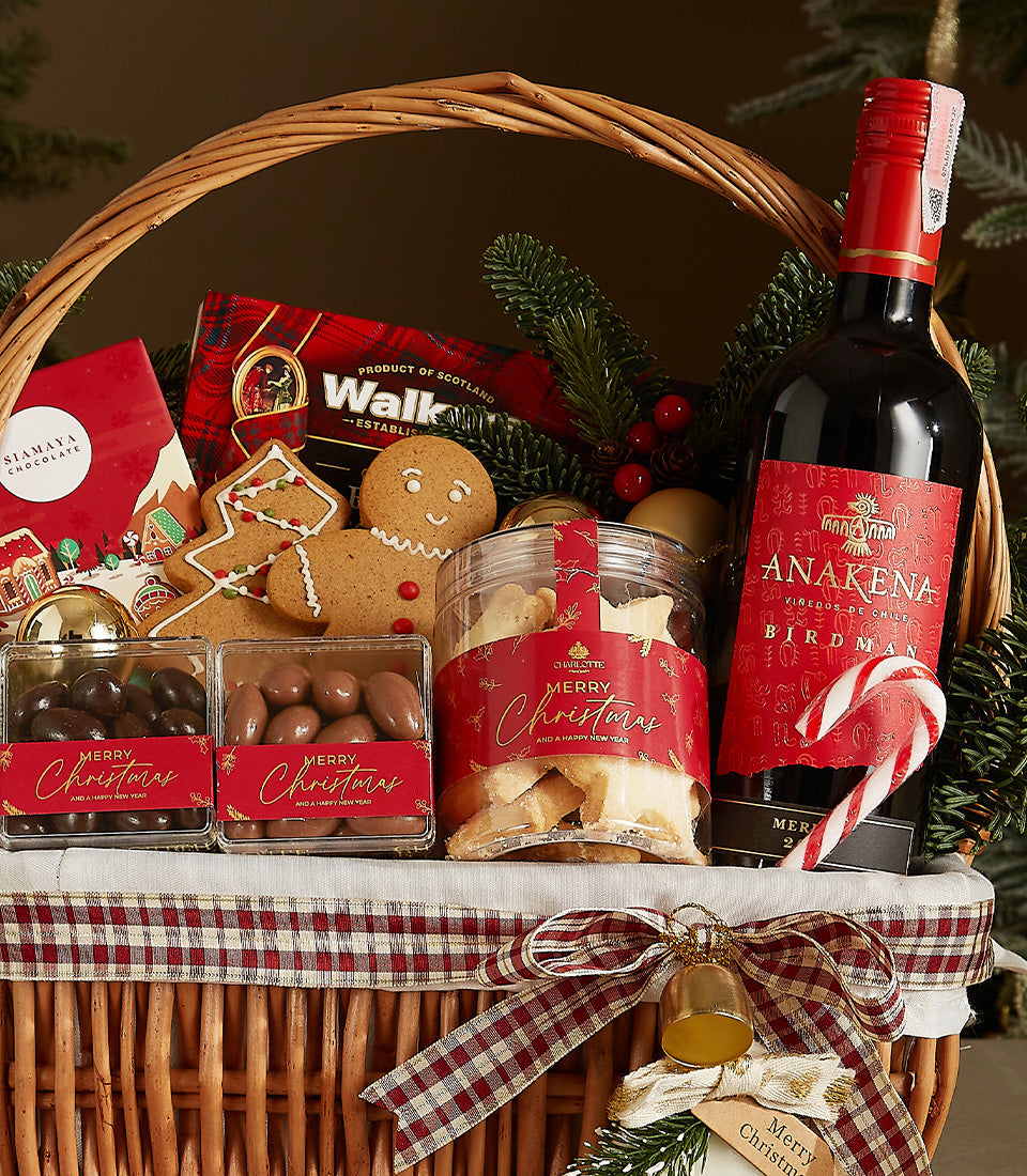 Festive wicker Christmas wine gift basket with red wine, gourmet shortbread, chocolate, nuts, and gingerbread treats, tied