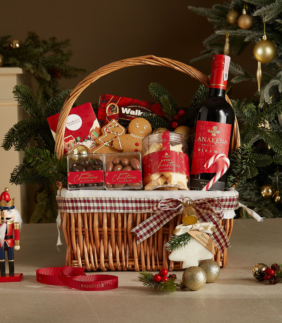 Festive Christmas wine gift basket with red wine, chocolate candies, gingerbread cookies, and shortbread in plaid-lined