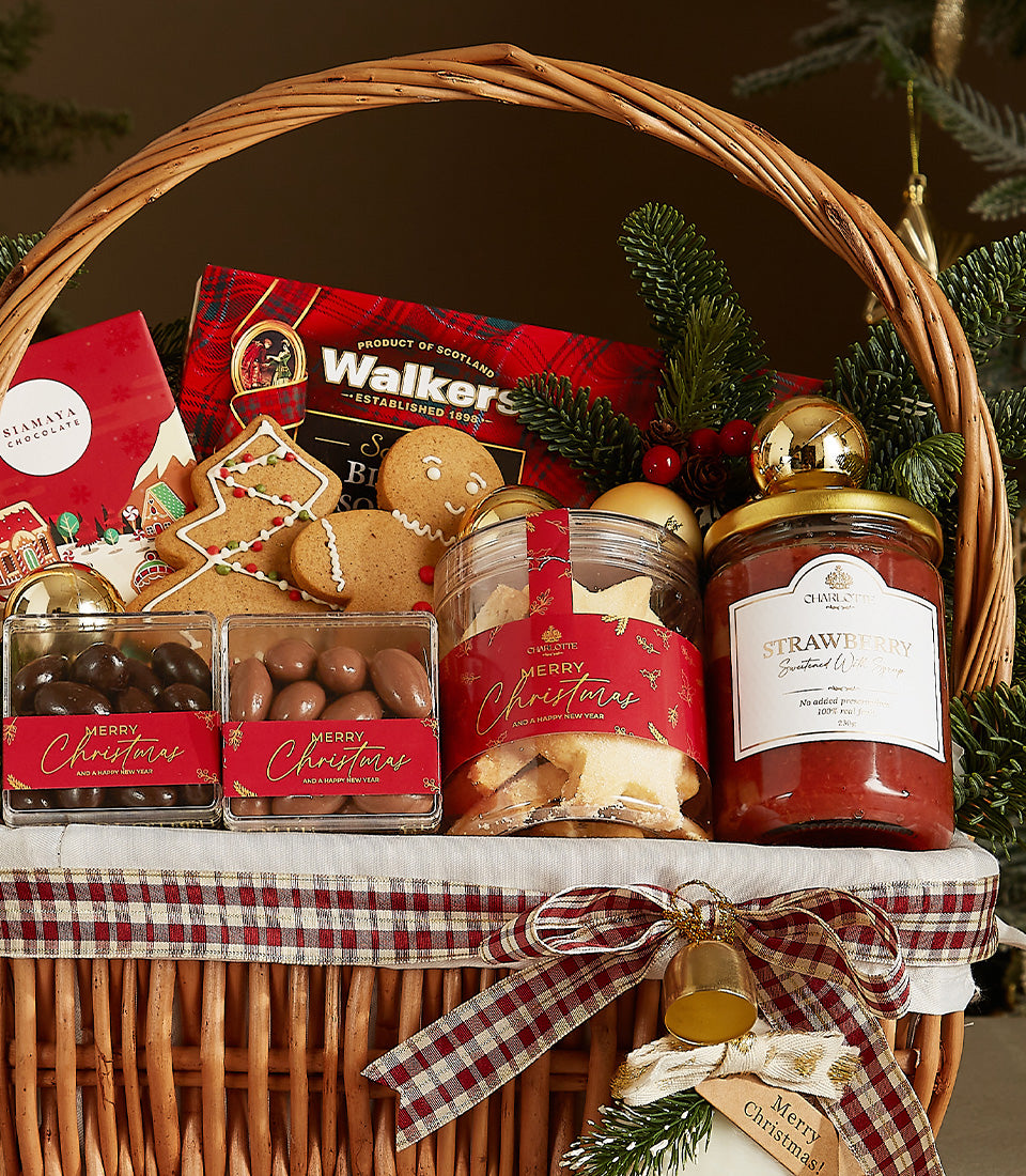 Woven wicker Christmas gift basket with red plaid ribbon, filled with gourmet treats including Walkers shortbread, artisan