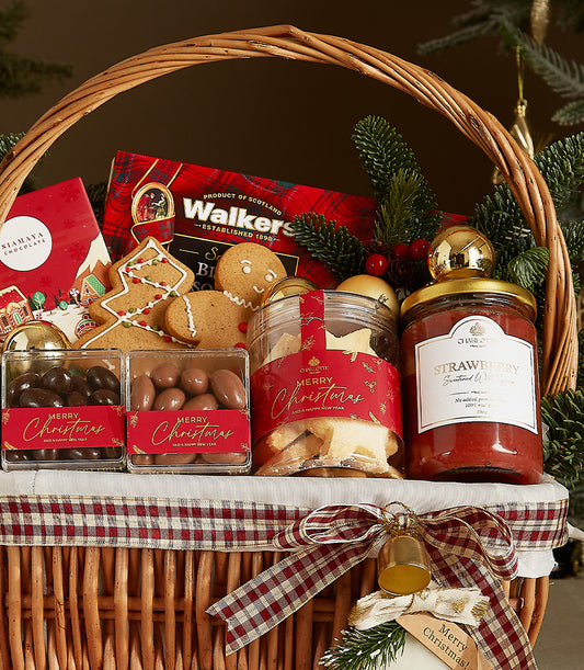 Woven wicker Christmas gift basket with red plaid ribbon, filled with gourmet treats including Walkers shortbread, artisan