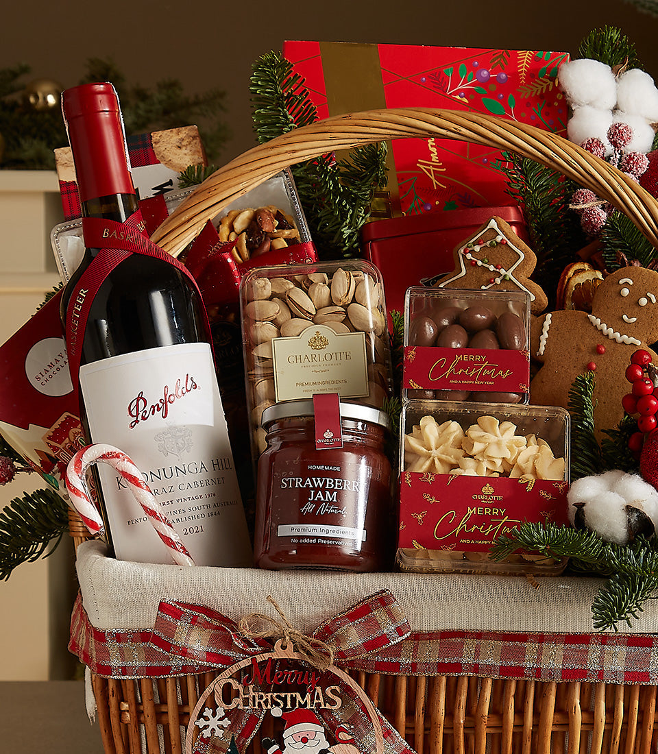 Woven wicker Christmas wine gift basket with red wine, gourmet chocolates, pistachios, jam, and festive treats tied with