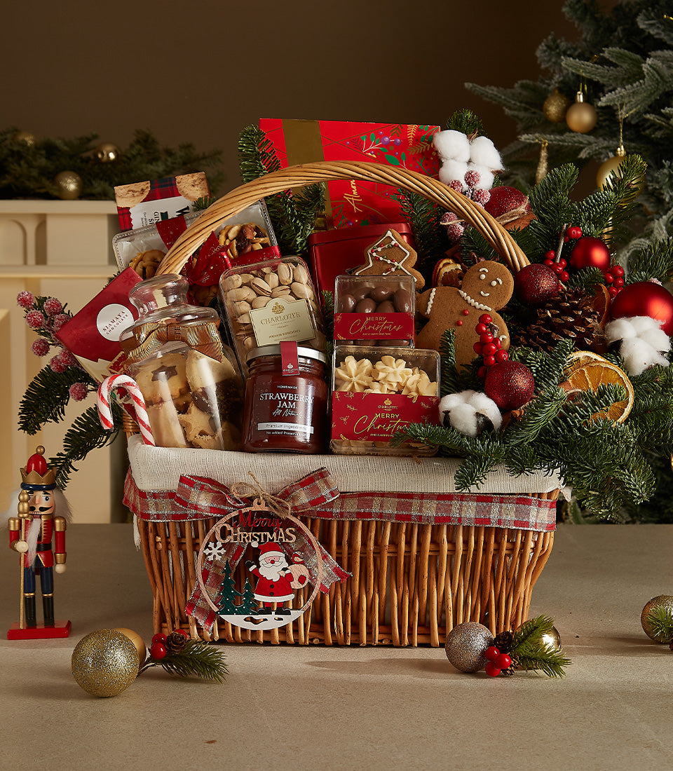 Festive wicker basket with gourmet treats, jam, nuts, cookies, chocolates, plaid ribbon and Christmas ornaments
