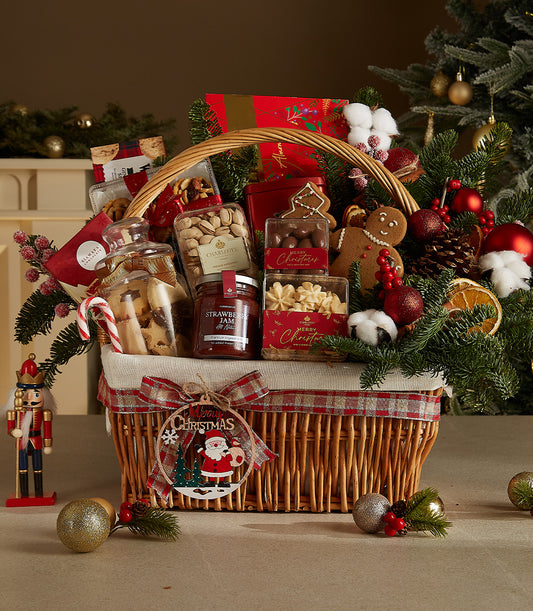 Festive wicker basket with gourmet treats, jam, nuts, cookies, chocolates, plaid ribbon and Christmas ornaments