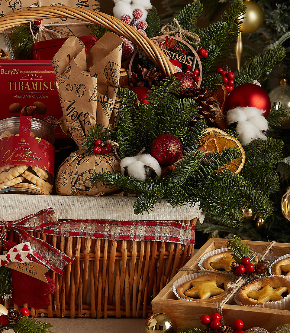 Festive Christmas hamper with red wine, tiramisu chocolate, cookies, and star tarts in wicker basket with plaid ribbon