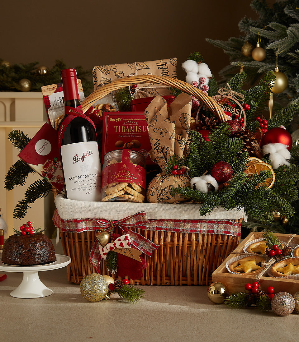 Wicker Christmas hamper with red wine, tiramisu chocolates, cookies, and festive treats tied with plaid ribbon