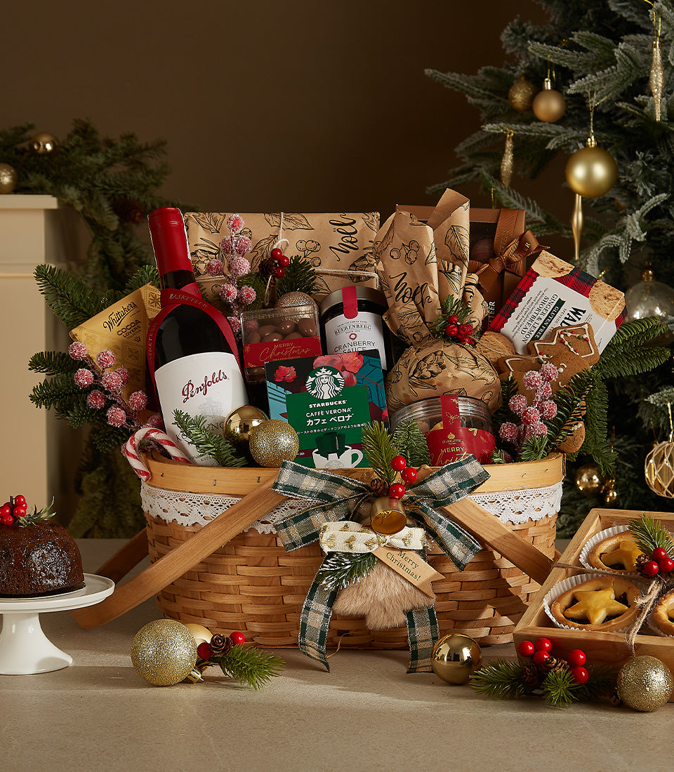 Festive red wine gift basket with cranberry sauce, coffee, shortbread, and holiday treats in woven basket with gold baubles