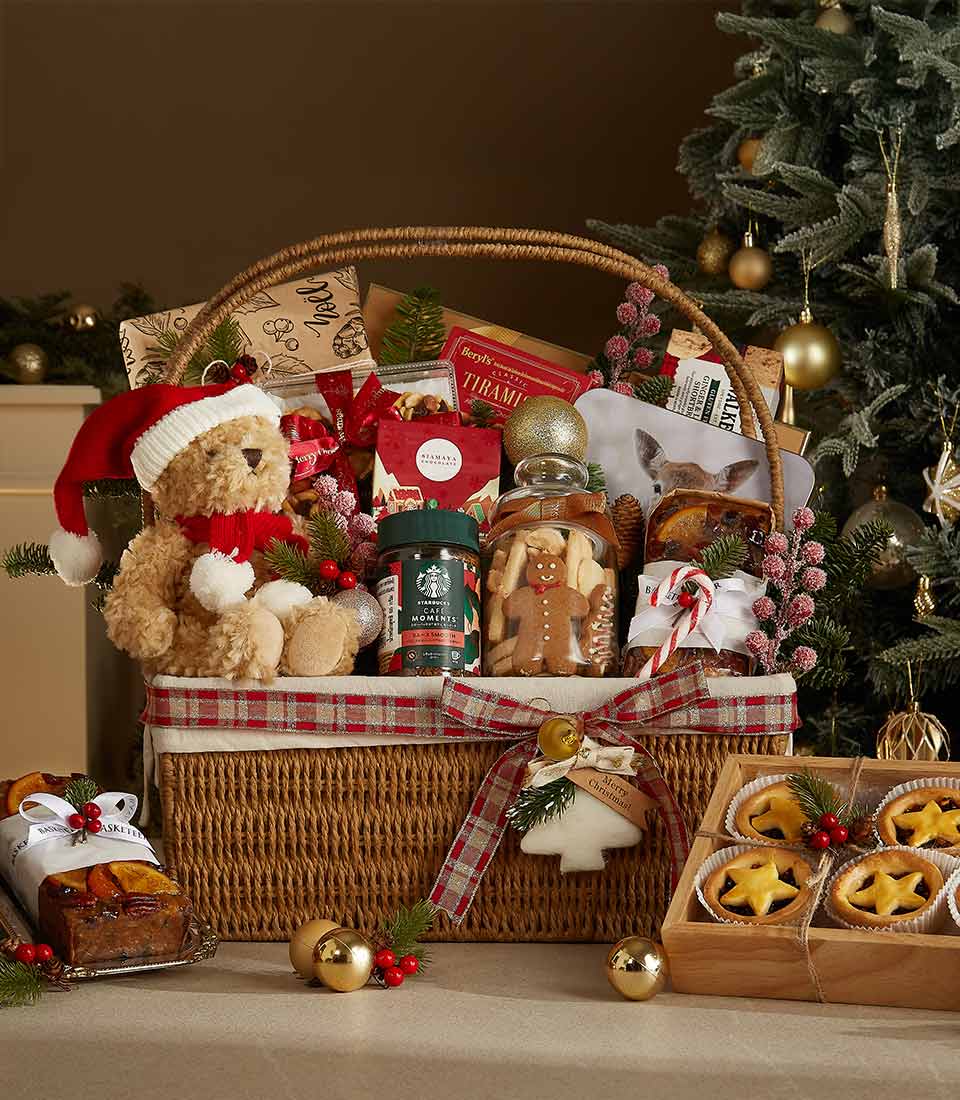 Wicker Christmas gift basket with plaid lining, teddy bear, gingerbread cookies, chocolates, and festive ornaments