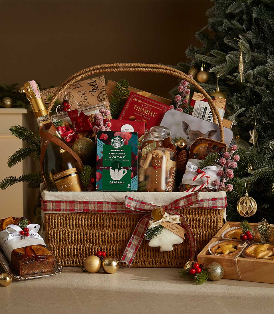 Festive Christmas gourmet hamper with sparkling wine, coffee, chocolates, and baked treats in wicker basket with red plaid