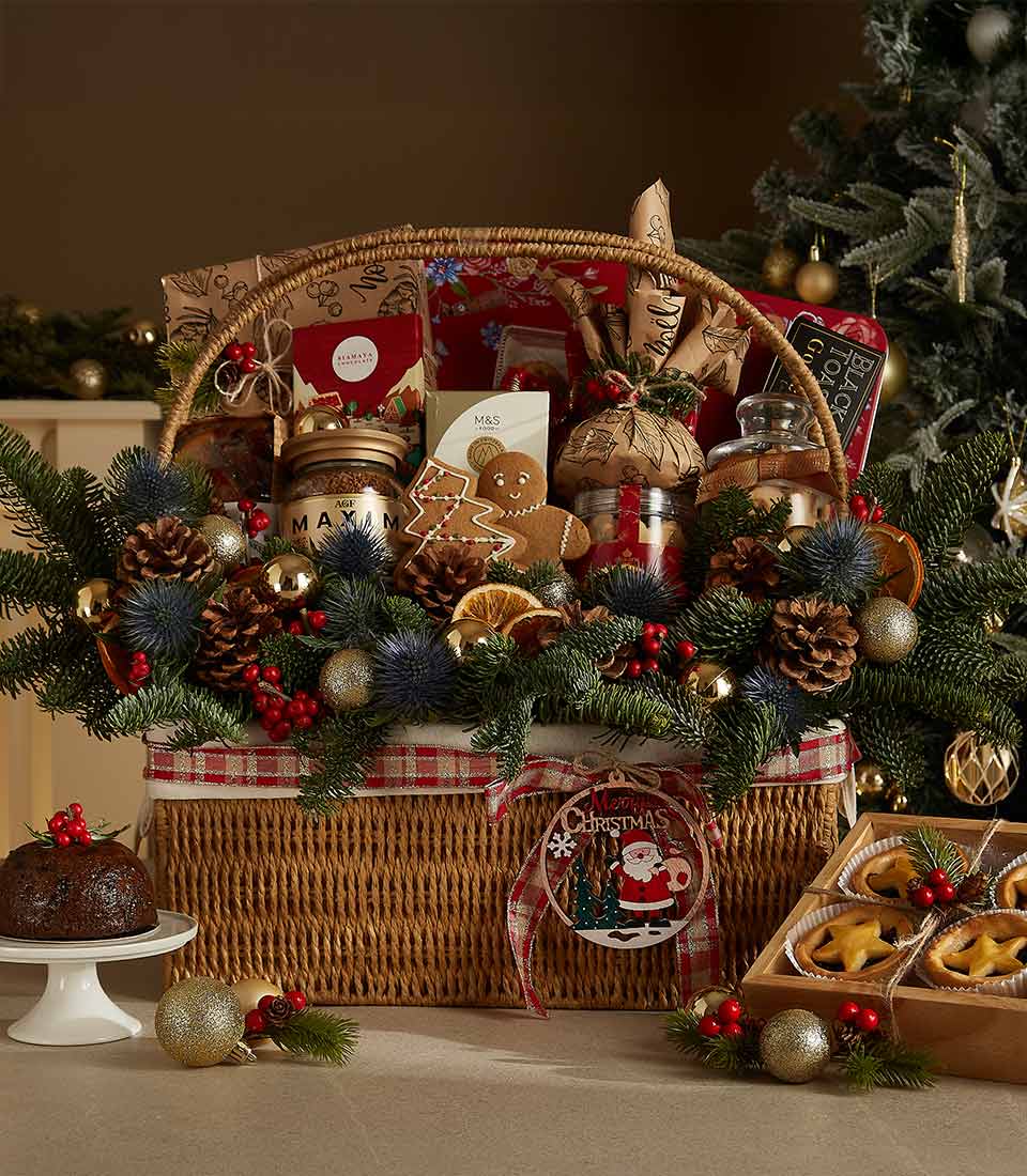 Wicker Christmas hamper with gourmet treats, gingerbread, chocolates, pine branches, and gold baubles for festive gifting