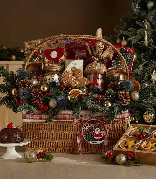 Wicker Christmas hamper with gourmet treats, gingerbread, chocolates, pine branches, and gold baubles for festive gifting