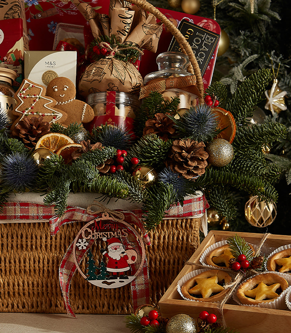 Wicker Christmas hamper with plaid ribbon, gingerbread cookies, mince pies, and festive greenery