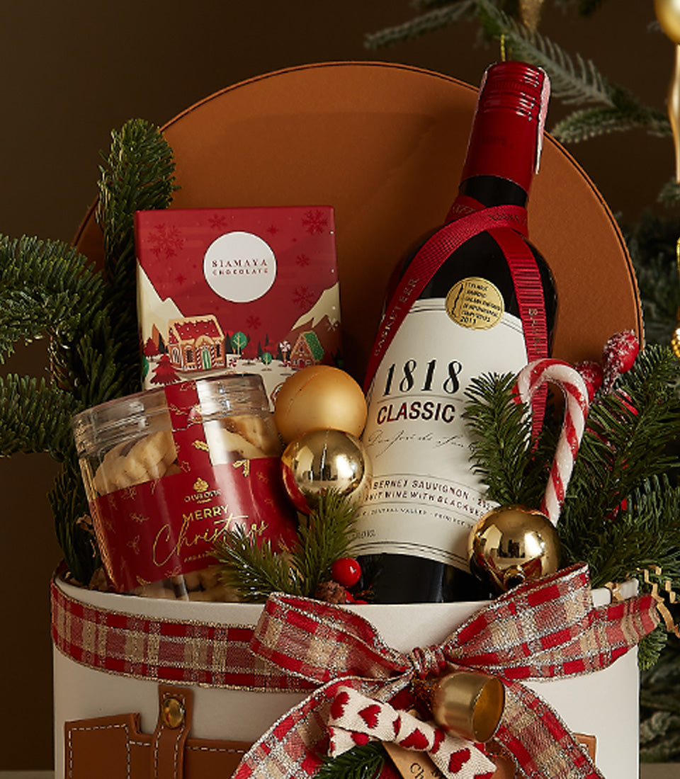 Luxury red wine gift basket with chocolates, Christmas cookies, and festive gold accents in white woven container