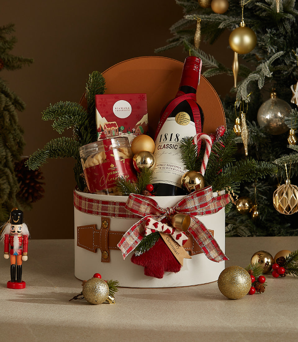 Red wine gift box with chocolate, cookies, and festive pine branches, red plaid ribbon and golden bell