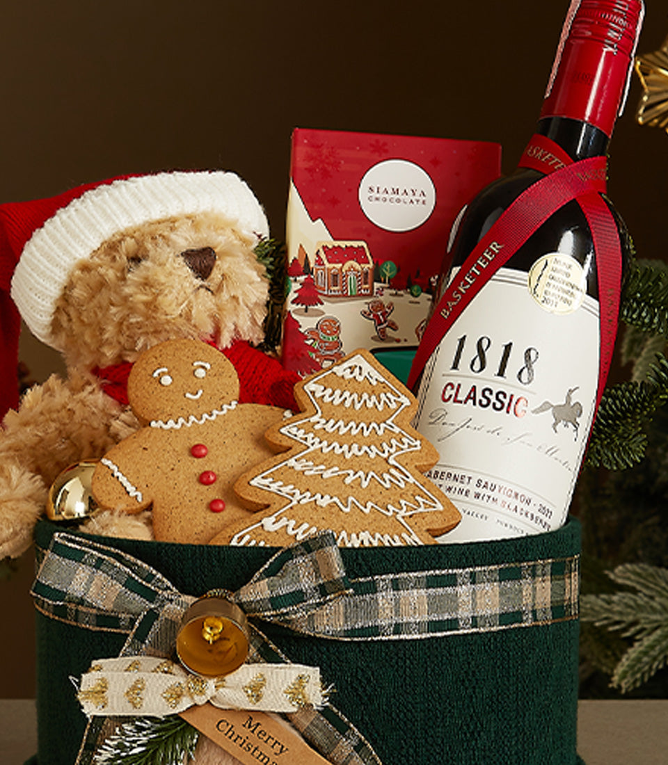 Luxury Christmas gift box with teddy bear in Santa hat, red wine, Siamaya chocolate, and gingerbread cookies in forest green