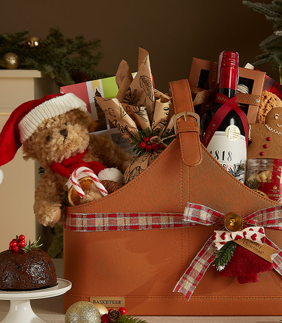 Festive brown leather wine gift basket with red wine, teddy bear in Santa hat, gingerbread, and holiday treats
