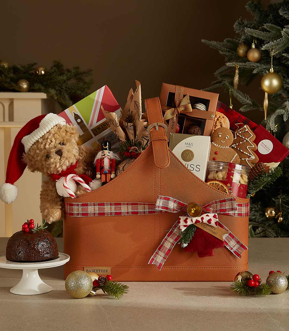 Brown leather Christmas gift basket with red plaid bow, filled with teddy bear, nutcracker, chocolates, and festive British