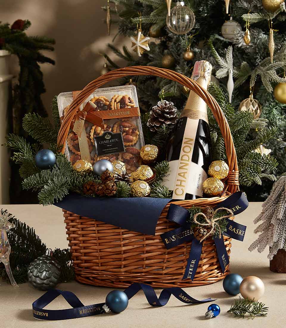 Woven wicker Christmas basket with Chandon champagne, gourmet pastries, gold Ferrero Rocher, and festive pine greenery