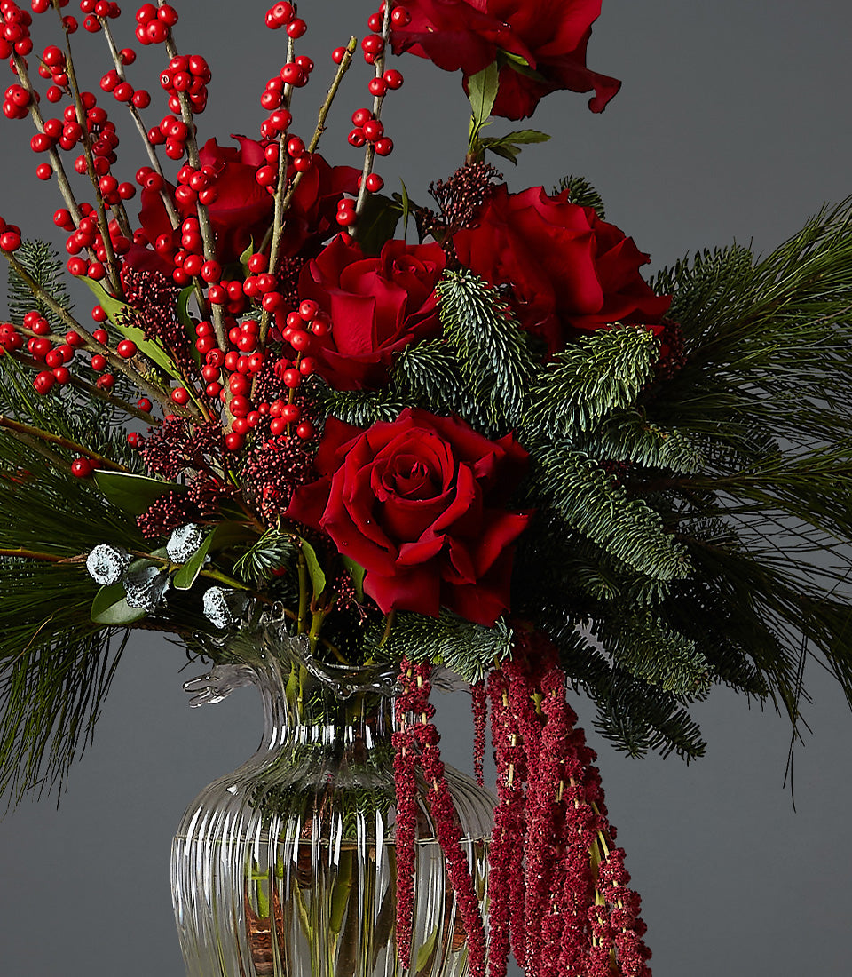 Festive red rose and winterberry arrangement in glass vase with evergreen foliage for Christmas gifting