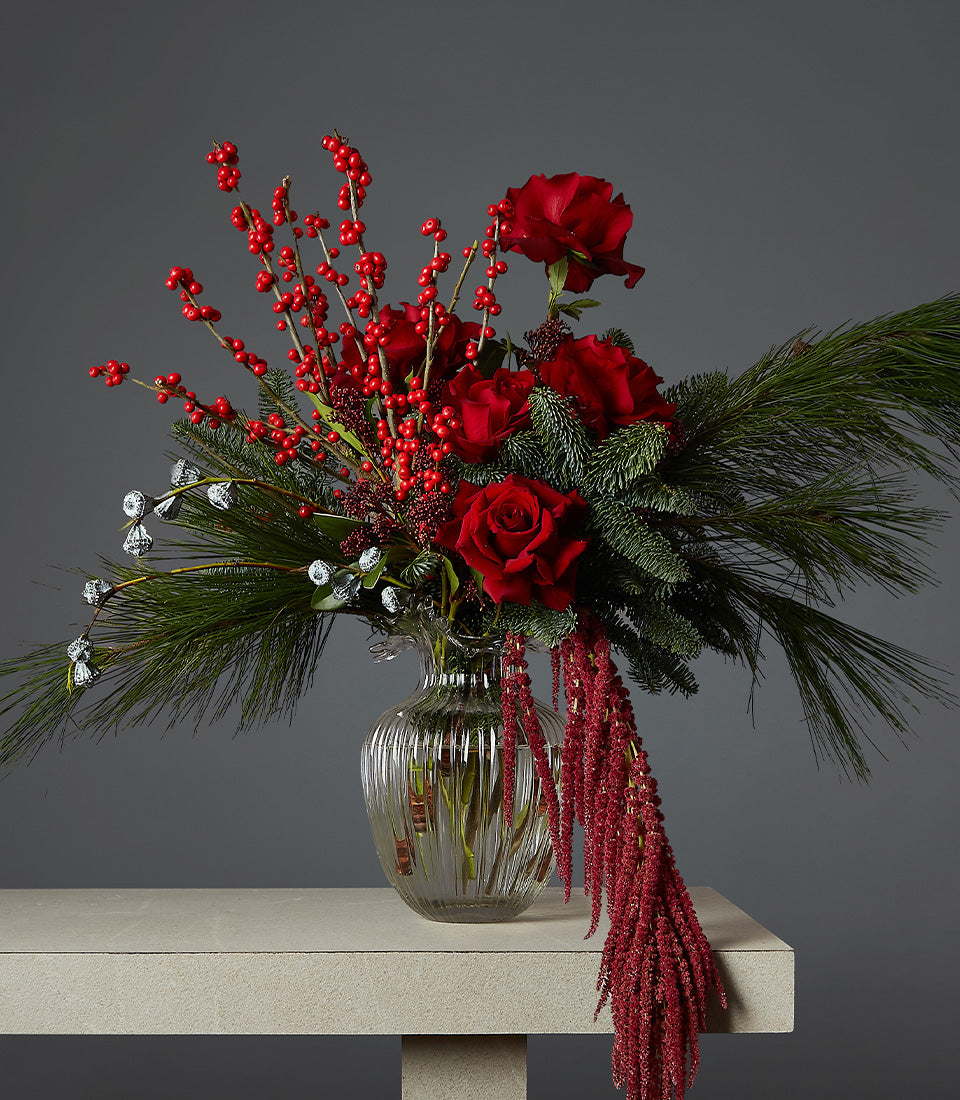 Elegant Christmas floral arrangement with deep red roses, hypericum berries, and cascading amaranthus in ribbed glass vase