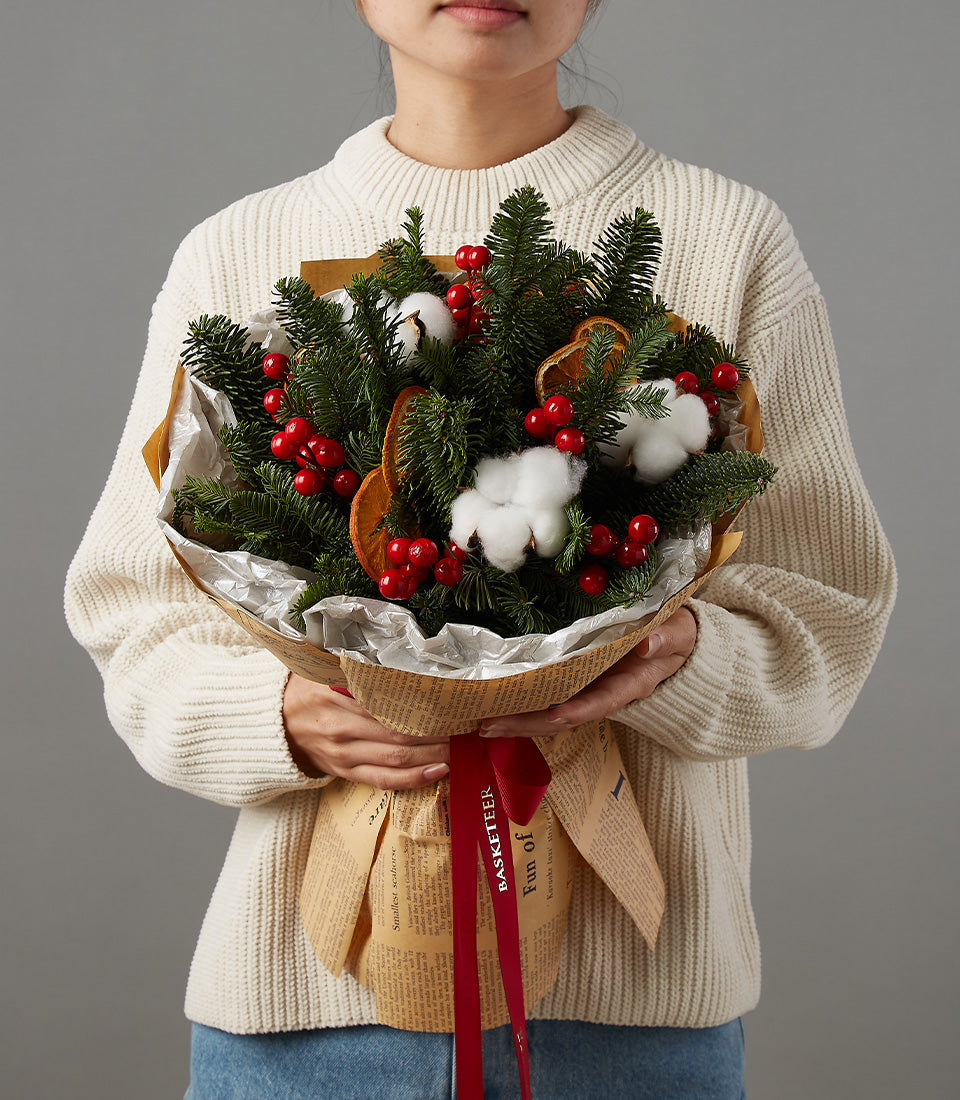 Festive Christmas bouquet with red berries, white cotton, and dried oranges in newspaper-print wrapping