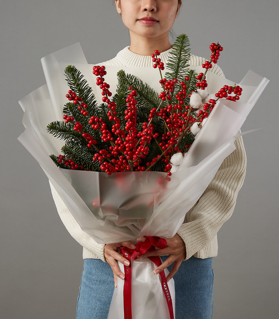 Festive red berries and pine Christmas bouquet with white cotton accents, wrapped in cream paper with red ribbon