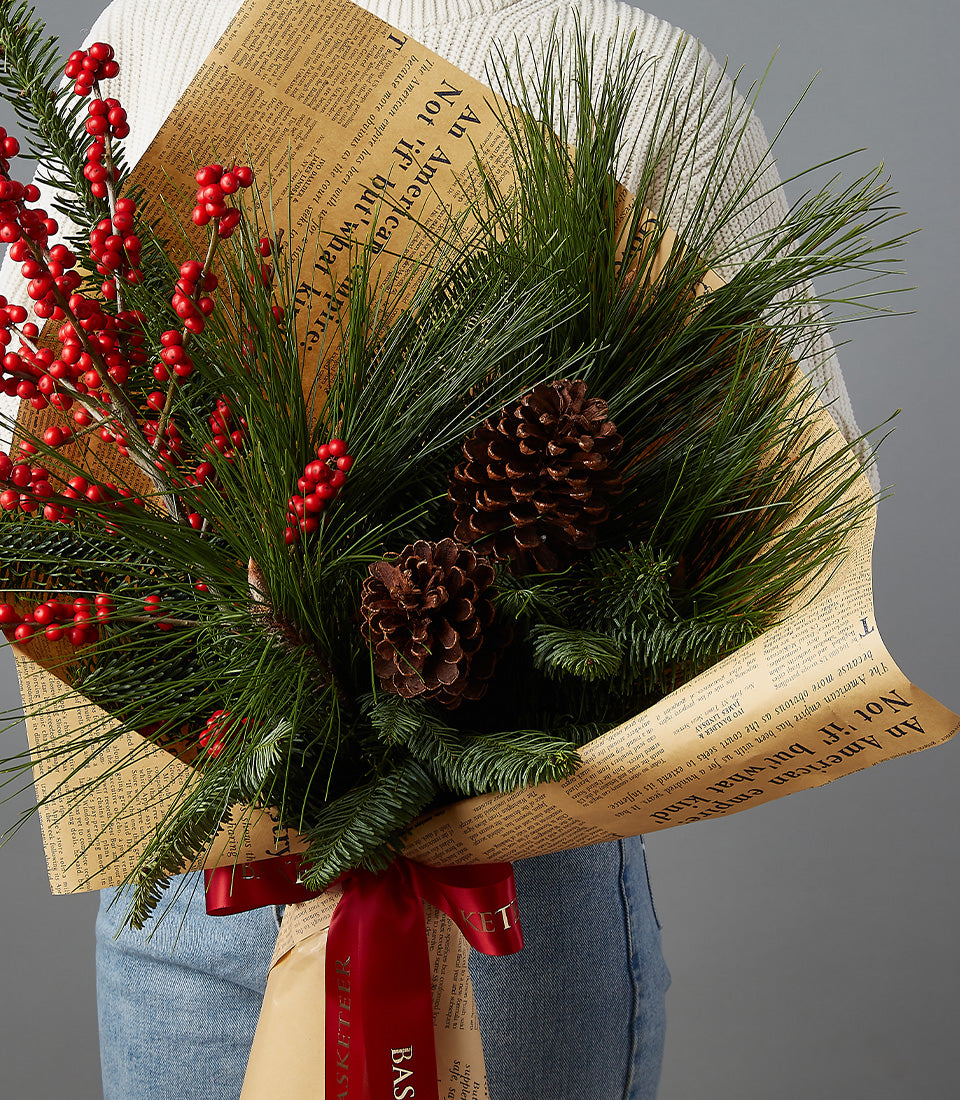 Festive Christmas bouquet with red berries, pine, and pinecones wrapped in brown paper with red ribbon
