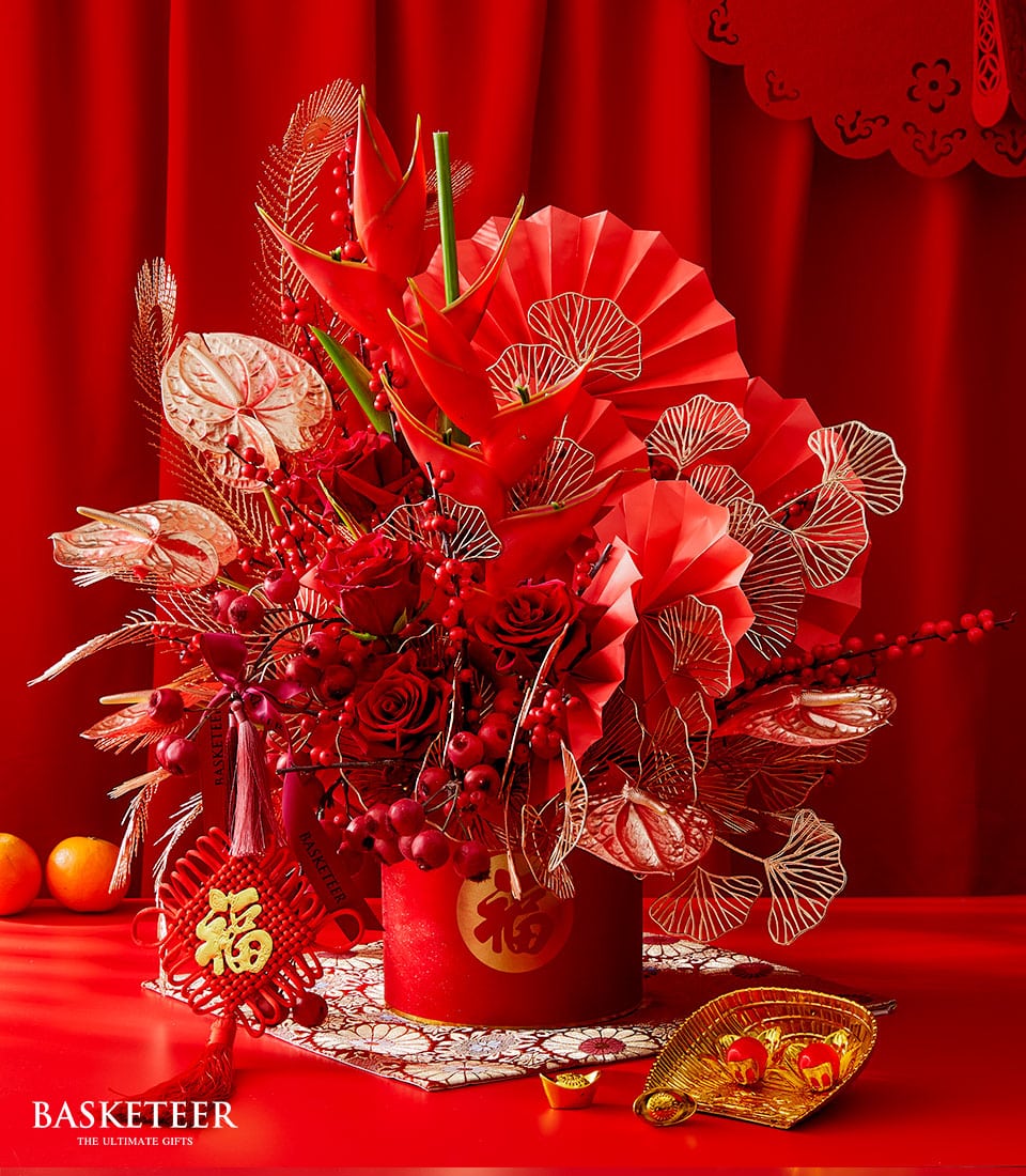 Red festive floral arrangement with roses and heliconia in cylindrical container, gold prosperity symbols for Chinese New