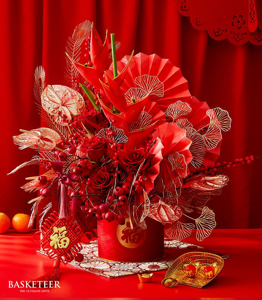 Red festive floral arrangement with roses and heliconia in cylindrical container, gold prosperity symbols for Chinese New