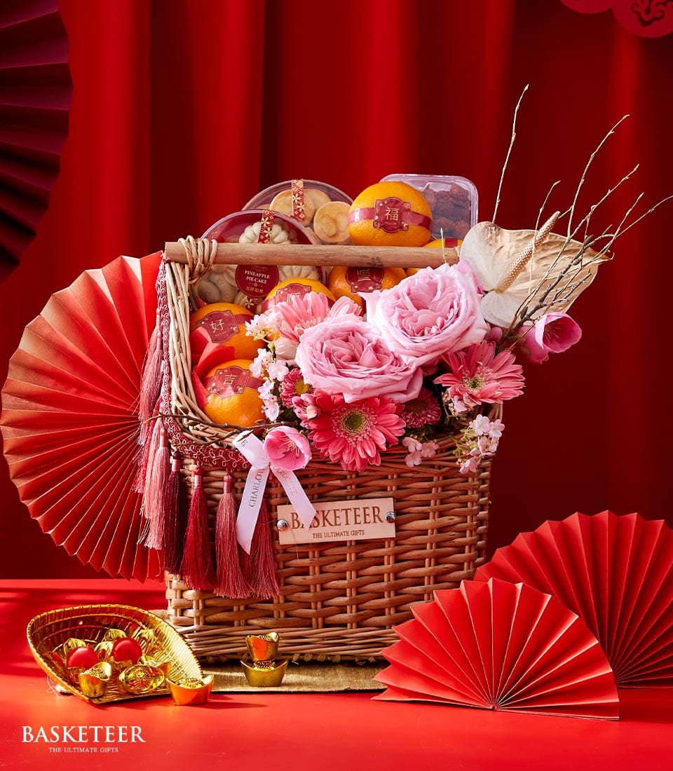 Luxury wicker gift basket with fresh pink roses, gerbera daisies, pineapple pie cake, mandarin oranges, and gold ingots for