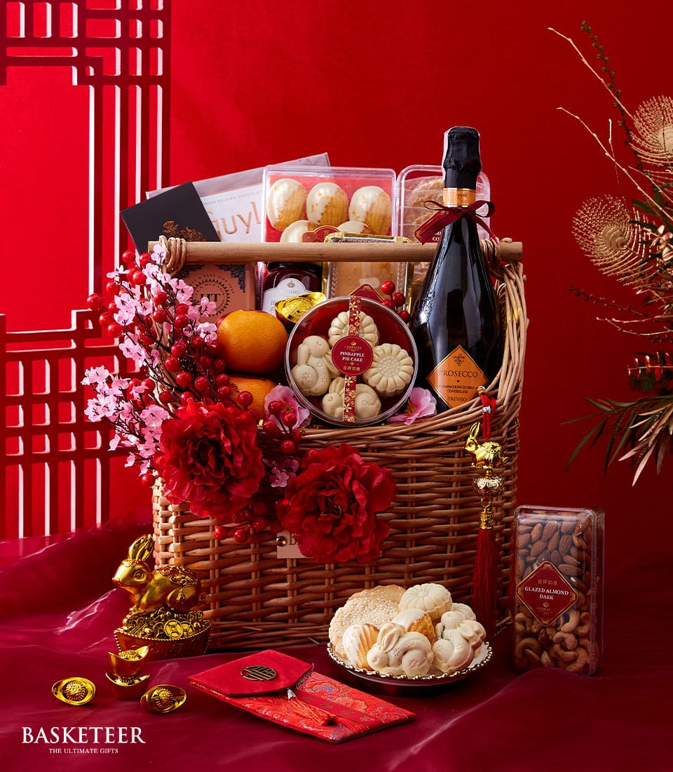 Lunar New Year gourmet basket with Prosecco, pineapple pie cake, fresh oranges, and festive red peony flowers on red