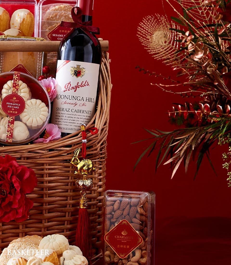 Lunar New Year wicker gift basket with Penfolds Shiraz, pineapple pie cakes, nuts, and gold rabbit charm on rich red