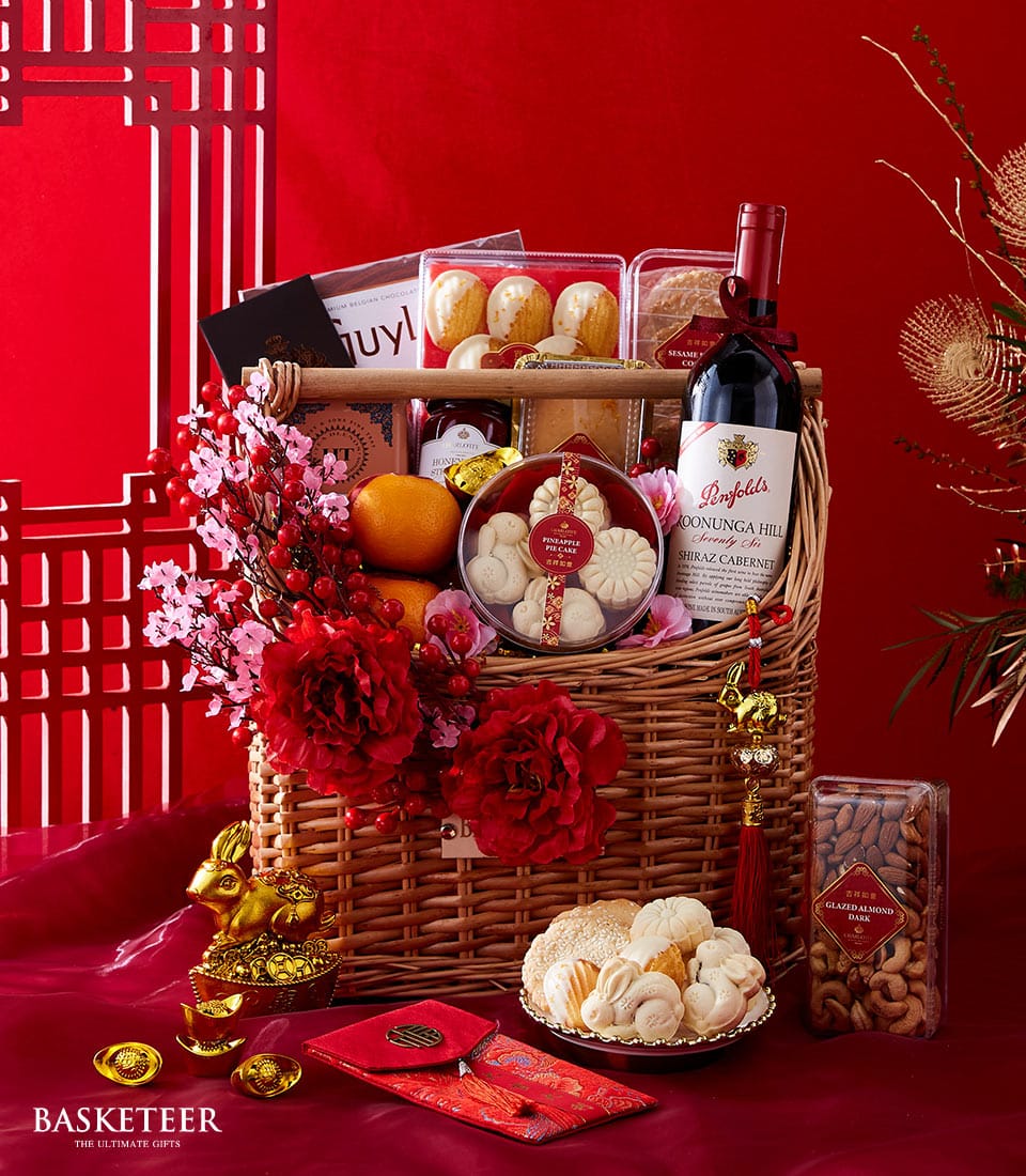 Lunar New Year wicker hamper with red wine, fresh oranges, artisan pastries, and festive gold accents on red background