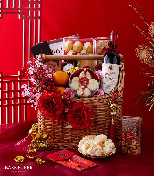 Lunar New Year wicker hamper with red wine, fresh oranges, artisan pastries, and festive gold accents on red background