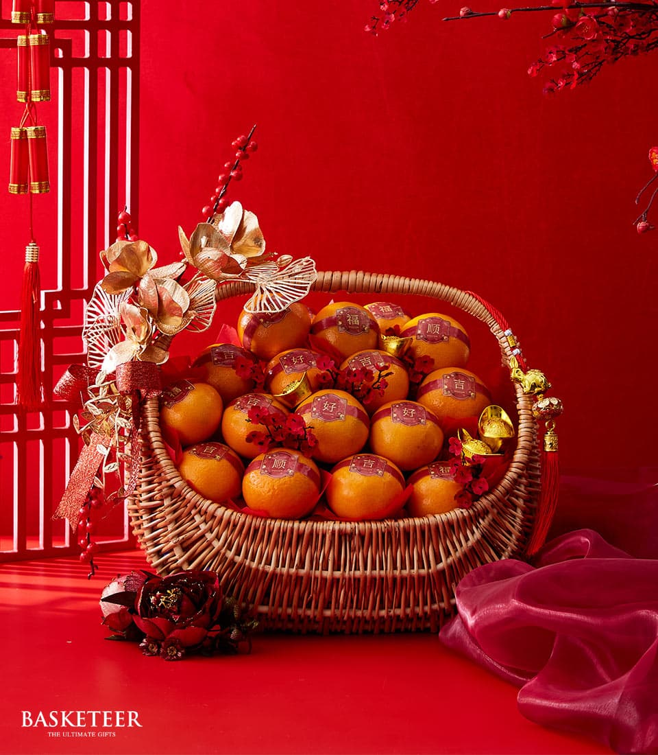Woven wicker basket filled with mandarin oranges and red tassel, golden florals for Chinese New Year gifting