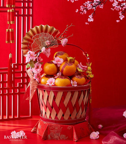Festive mandarin oranges gift basket with red woven design, gold character tags, and cherry blossoms for Chinese New Year