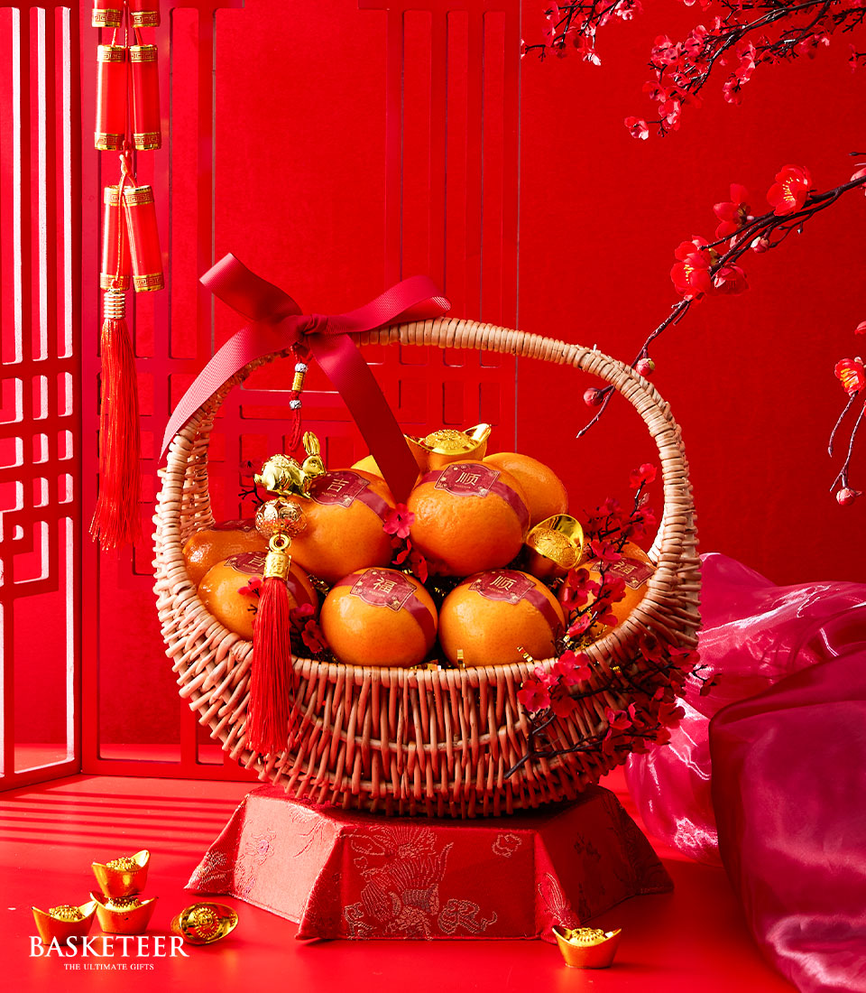 Festive mandarin orange wicker basket with red satin bow, gold charms, and red lucky stickers for Chinese New Year