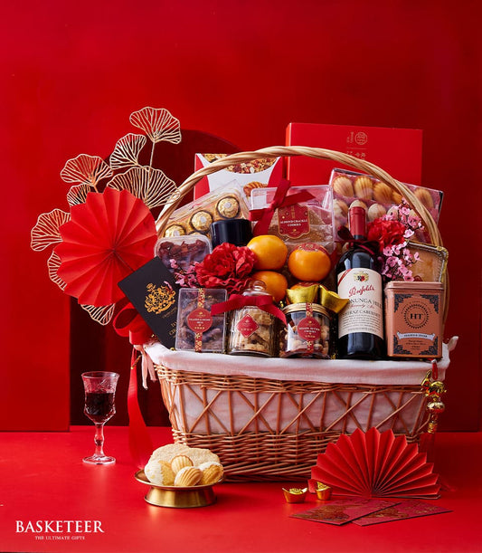 Luxury Chinese New Year wine and treats hamper with red wine, oranges, gourmet cookies, and festive gold ornaments in woven