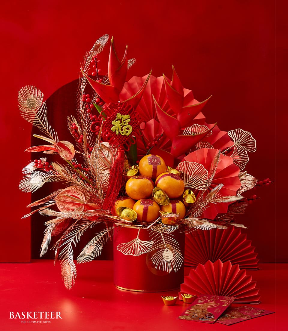 Lunar New Year flowers gift with red cylindrical vase, golden decorative sprays, mandarin oranges, and lucky gold ingots