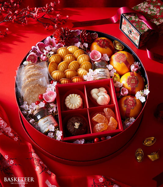Lunar New Year red gift basket with madeleines, cookies, oranges, bird's nest, and artisan pastries among cherry blossoms