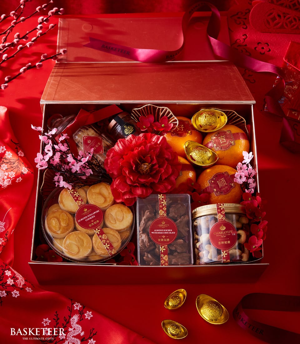 Luxurious red Lunar New Year gift box with golden oranges, almond cookies, chocolate treats, and festive peonies