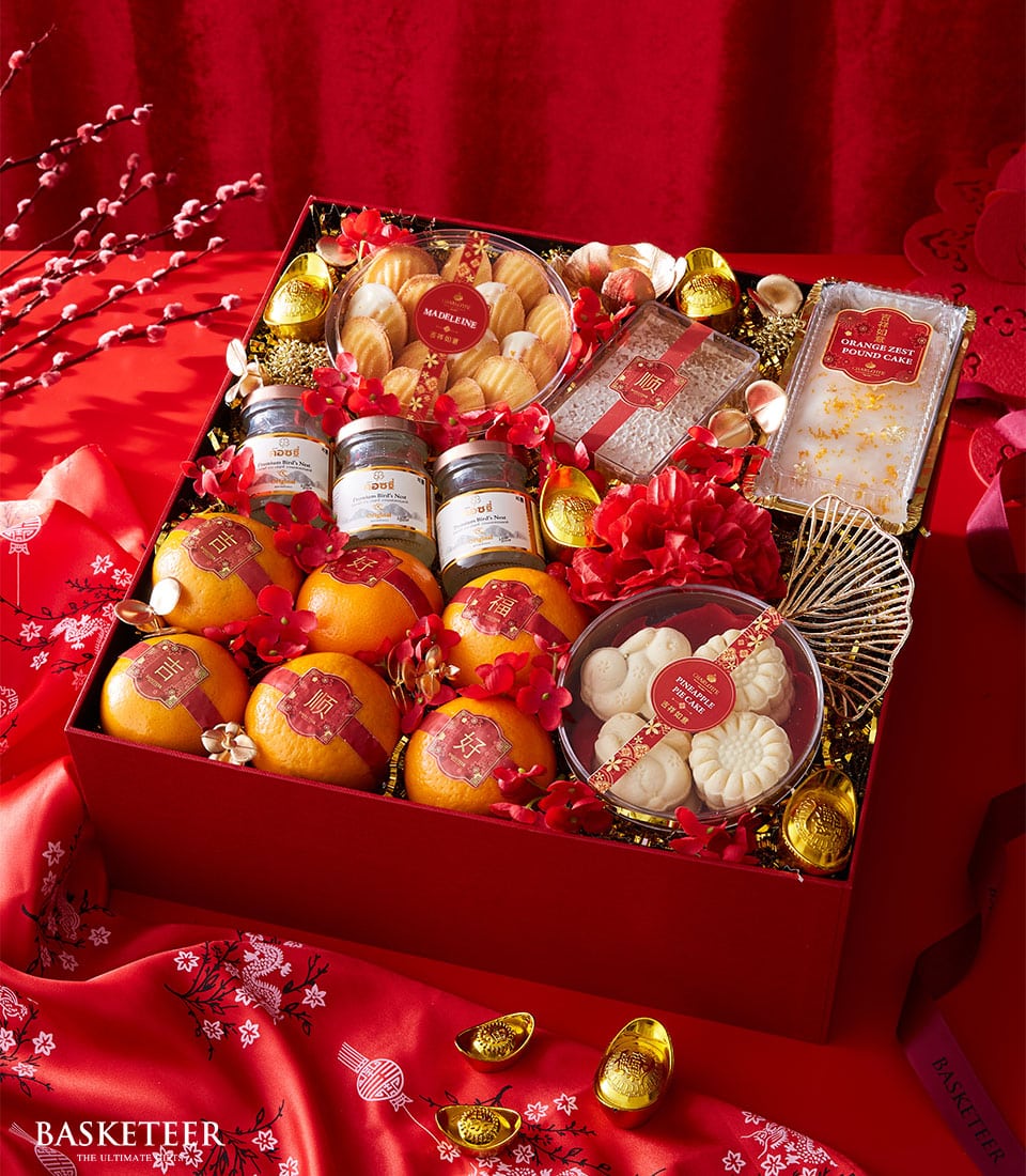 Festive gift box with mandarin oranges, bird's nest drink, and artisan cakes on gold shredded paper with lucky charms