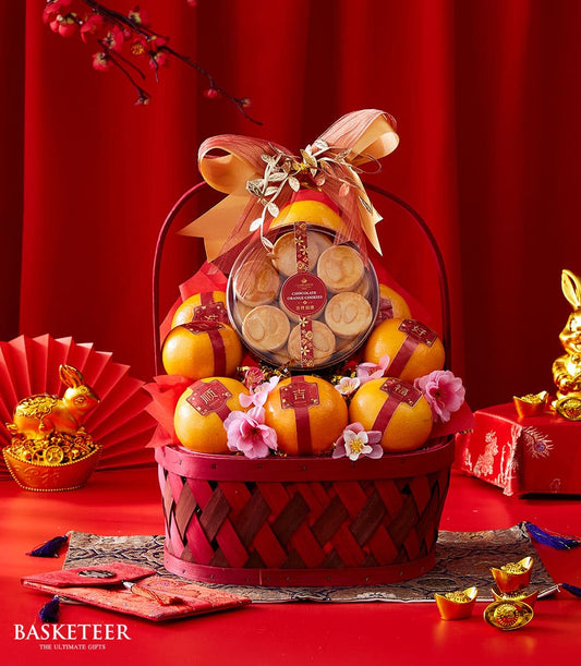 Red woven basket with mandarin oranges, chocolate orange cookies, gold ribbon, and lucky charms for Chinese New Year gifting