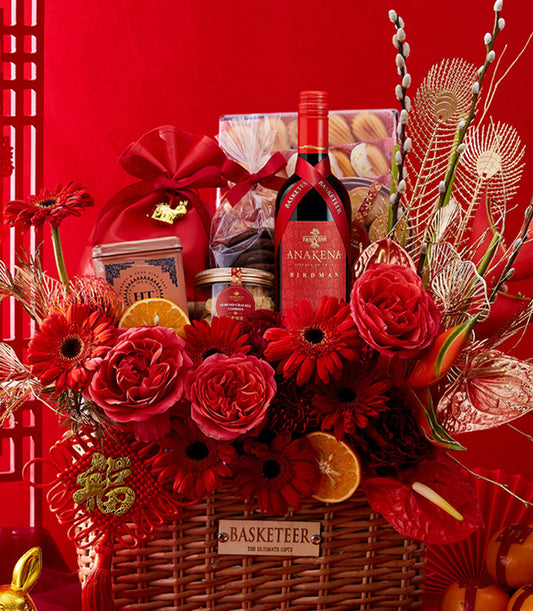 Lunar New Year wine and treats gift basket with red wine, gourmet cookies, and red roses in gold-accented woven hamper