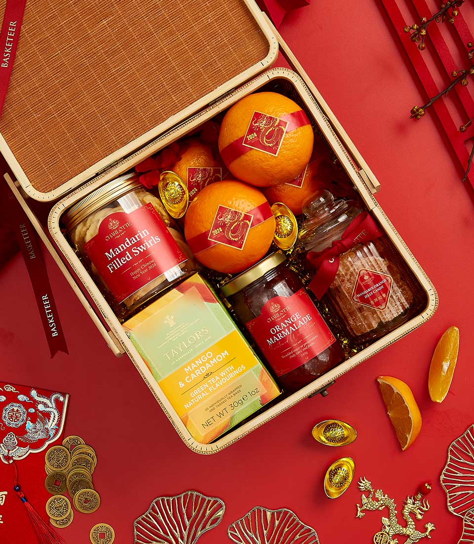 Basketeer Lunar New Year gift in woven basket: oranges with festive stickers, mandarin swirl cookies, marmalade, and aromatic tea. Perfect premium hamper delivery in Thailand.