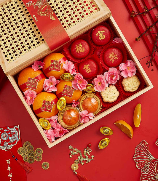 Festive Chinese New Year gift basket with red wrapped oranges, golden ingots, red celebration cakes, and persimmons on