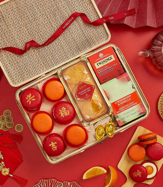 Festive Chinese New Year gift basket with mandarin pound cake, fortune macarons, and premium teas on red background