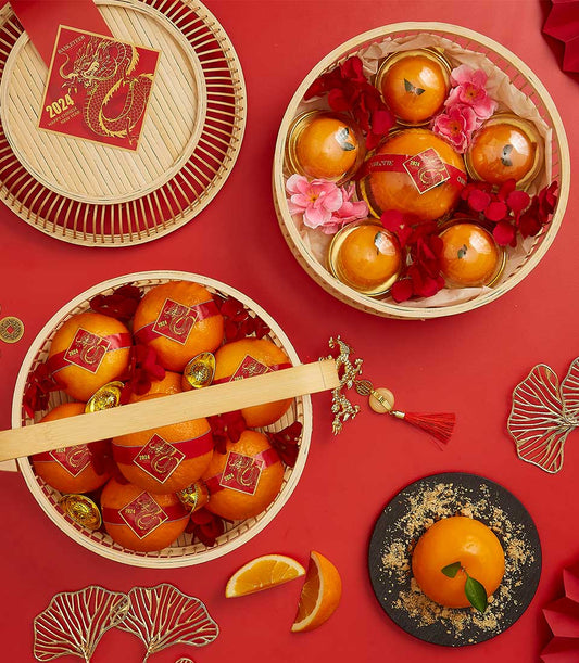 Festive CNY gift basket with mandarin oranges, lucky gold coins, and orange-shaped dessert on red background