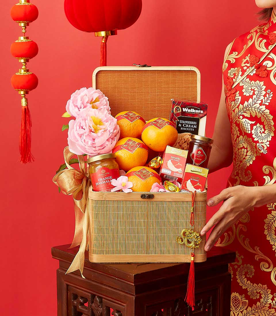 Festive Lunar New Year gift basket with mandarins, marmalade, biscuits, and pink peonies against red lantern backdrop